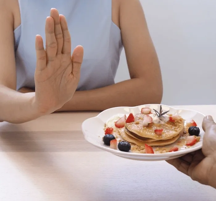 A woman raises her hand to refuse a plate of pancakes with berries