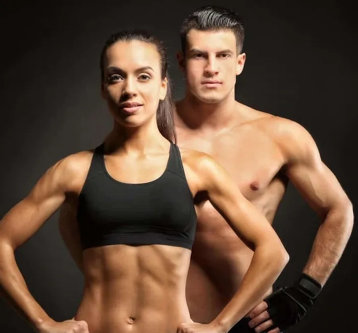 A fit man and woman in workout clothes pose with arms crossed