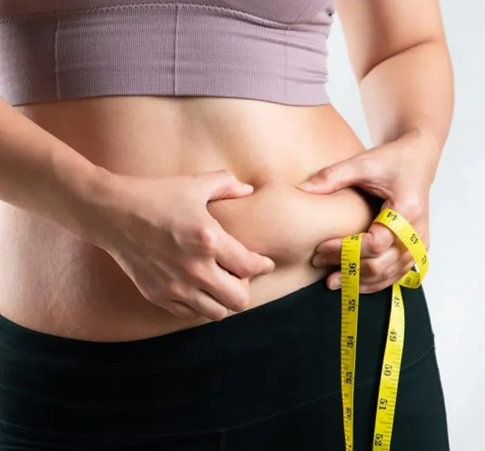 A woman in a sports top wraps a yellow measuring tape around her waist