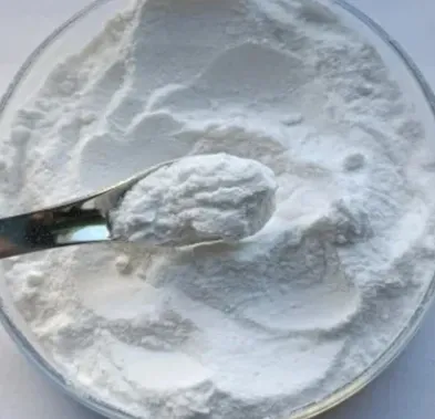 A metal scoop lifting fine white powder from a glass lab dish